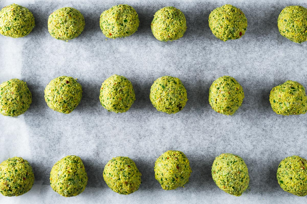 Uncooked falafel balls arranged on a parchment-lined baking sheet viewed from above.