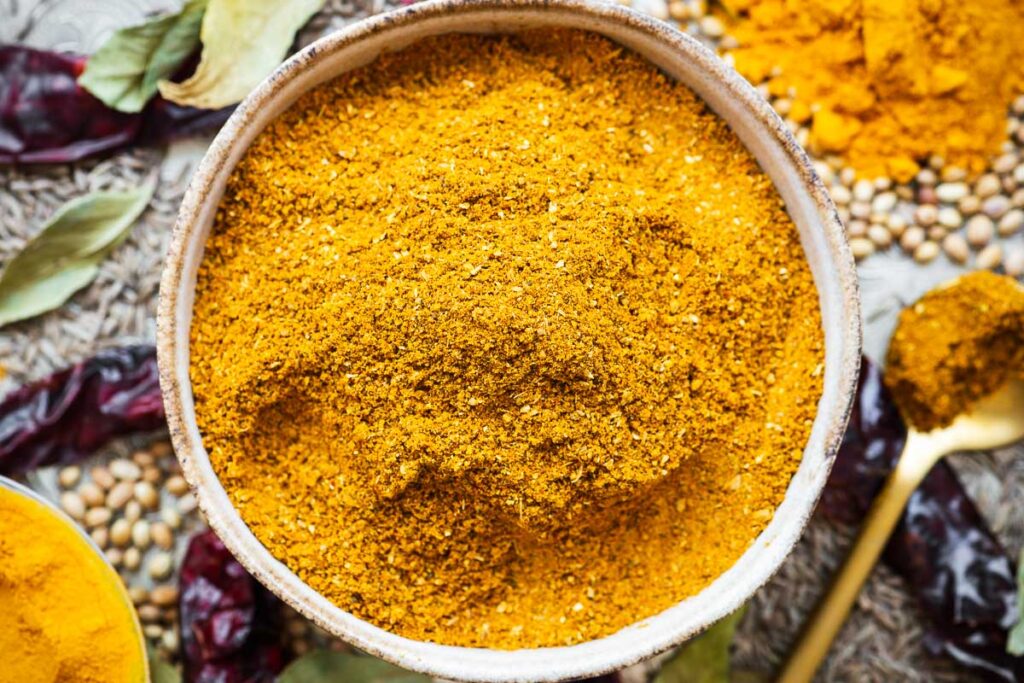The best curry powder substitute in a bowl with a golden spoon surrounded with ingredients.
