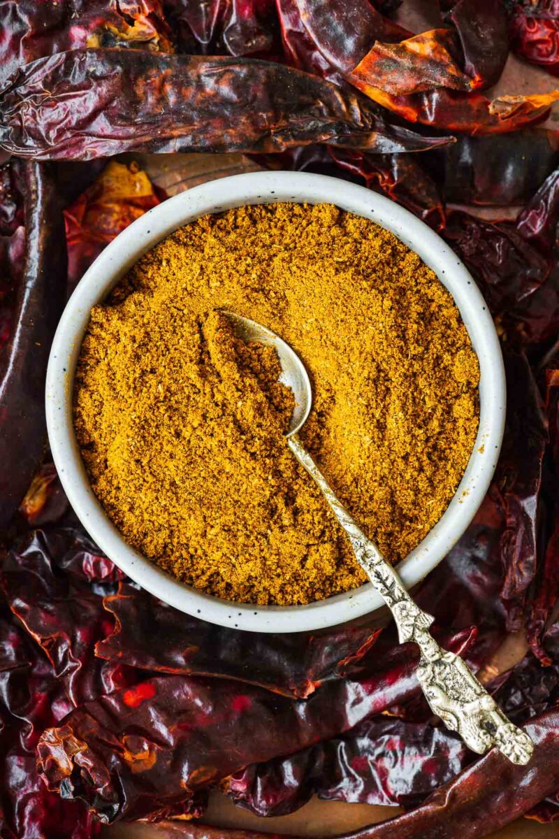 The best madras curry powder substitute in a ceramic bowl surrounded by dried red chillies.