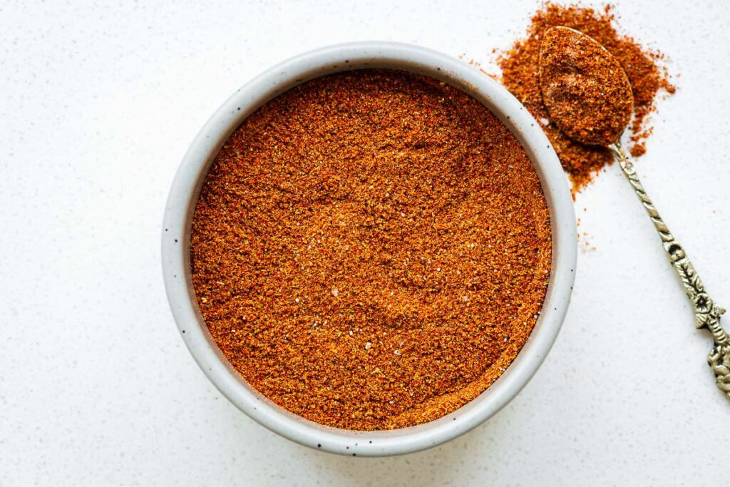 A horizontal image of a bowl with the simple harissa powder substitute consisting of cayenne pepper, smoked paprika, ground cumin, ground coriander, garlic powder and salt.