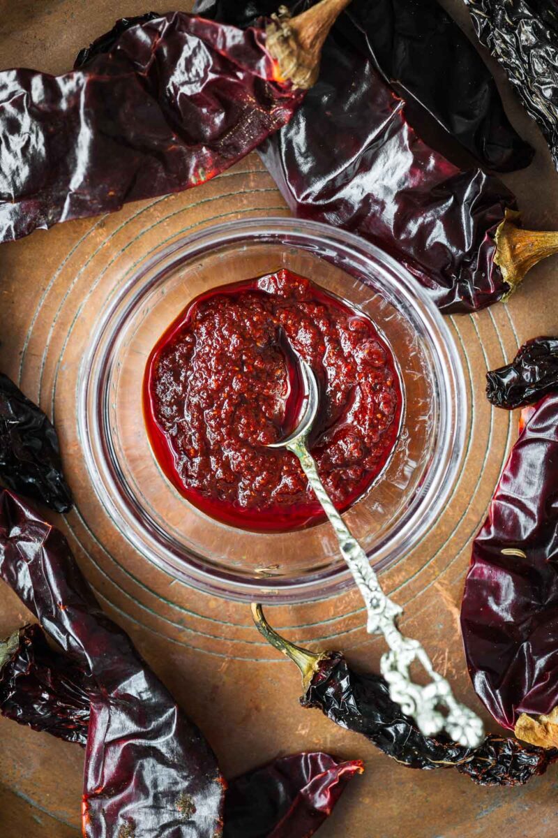 Harissa paste made by rehydrating harissa powder with water and olive oil in a glass bowl surrounded by dried red  chiles.