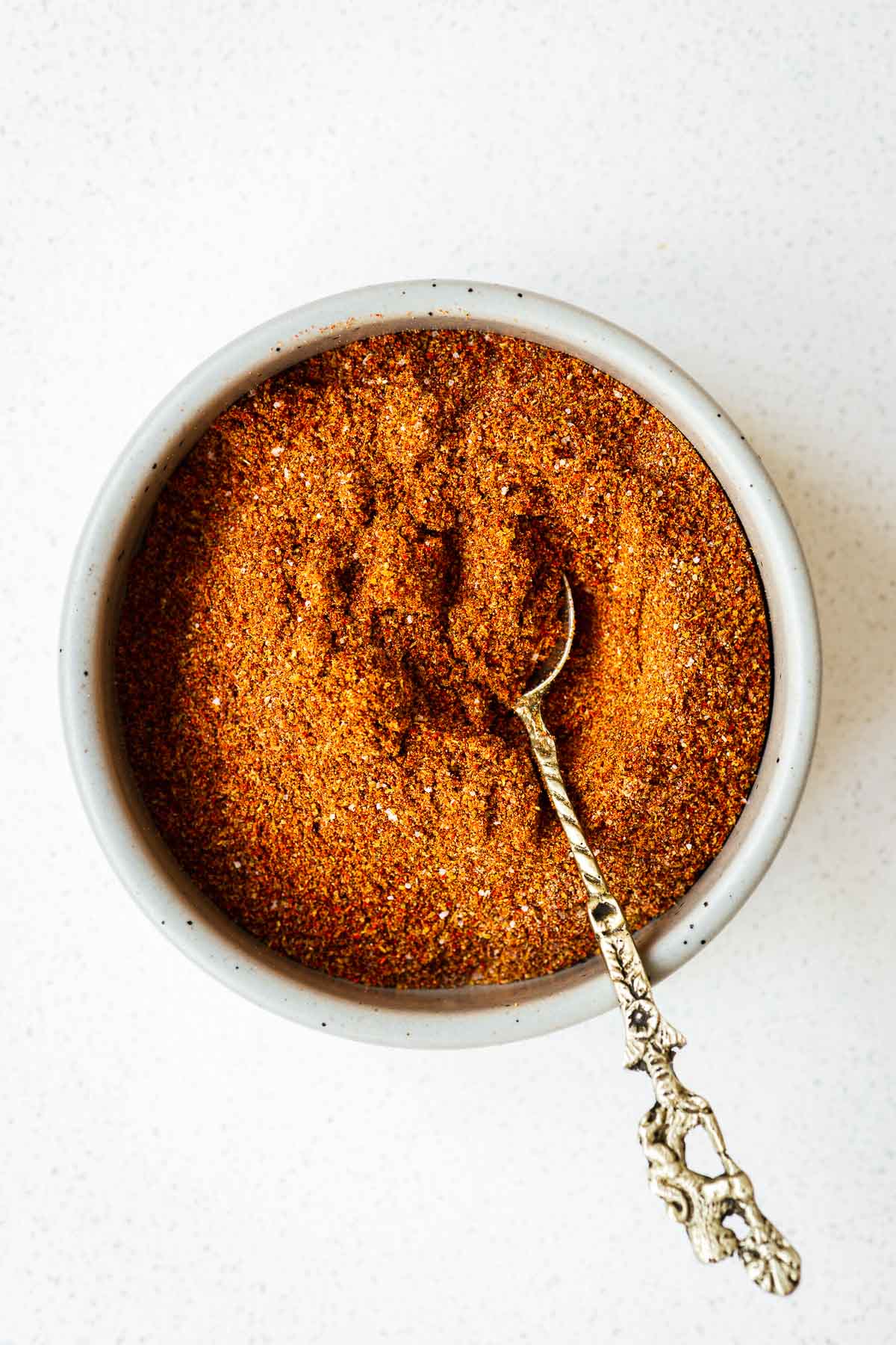 A bowl of harissa powder substitute (a simple ground spice blend) and a small teaspoon.