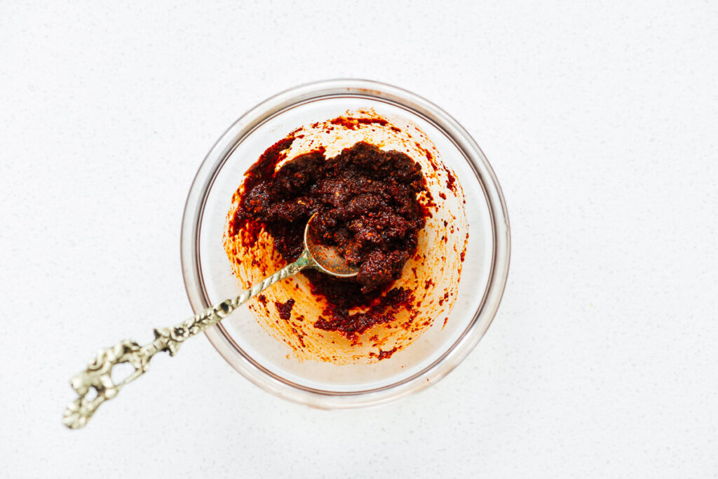 Harissa powder mixed with water in a small glass bowl viewed from above.