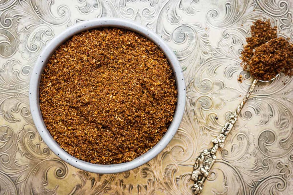 Homemade garam masala substitute with a teaspoon on a silver detailed tray.