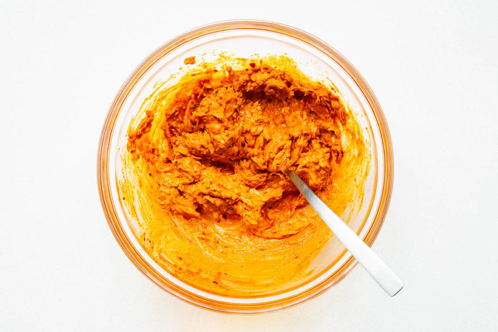 Top down view of a glass mixing bowl with harissa compound butter.