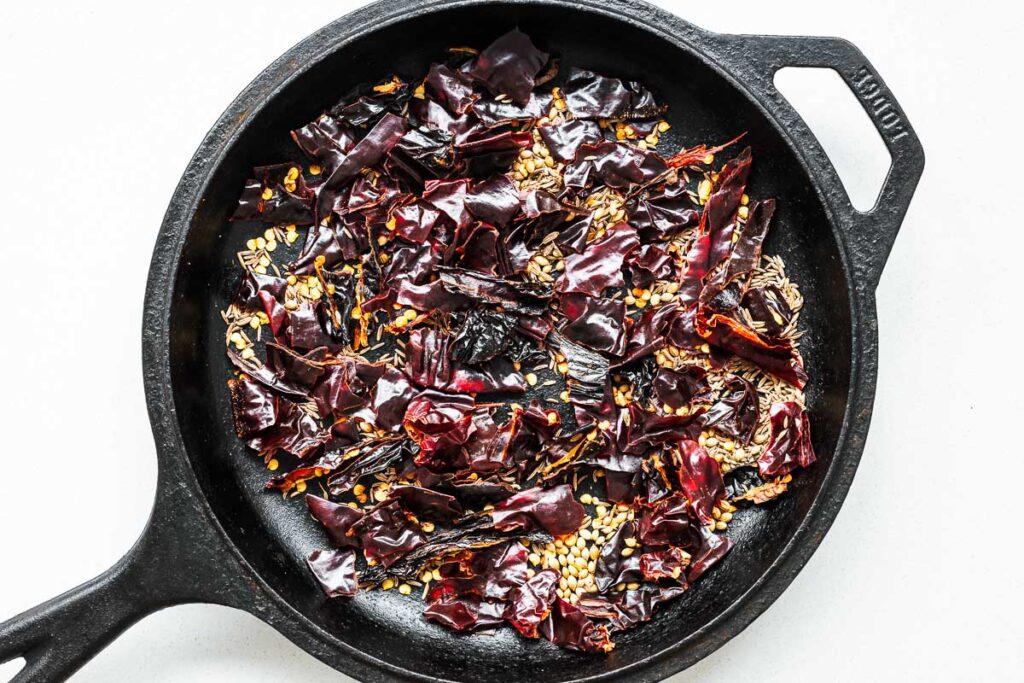 Dried chile peppers and spices in a skillet for toasting.