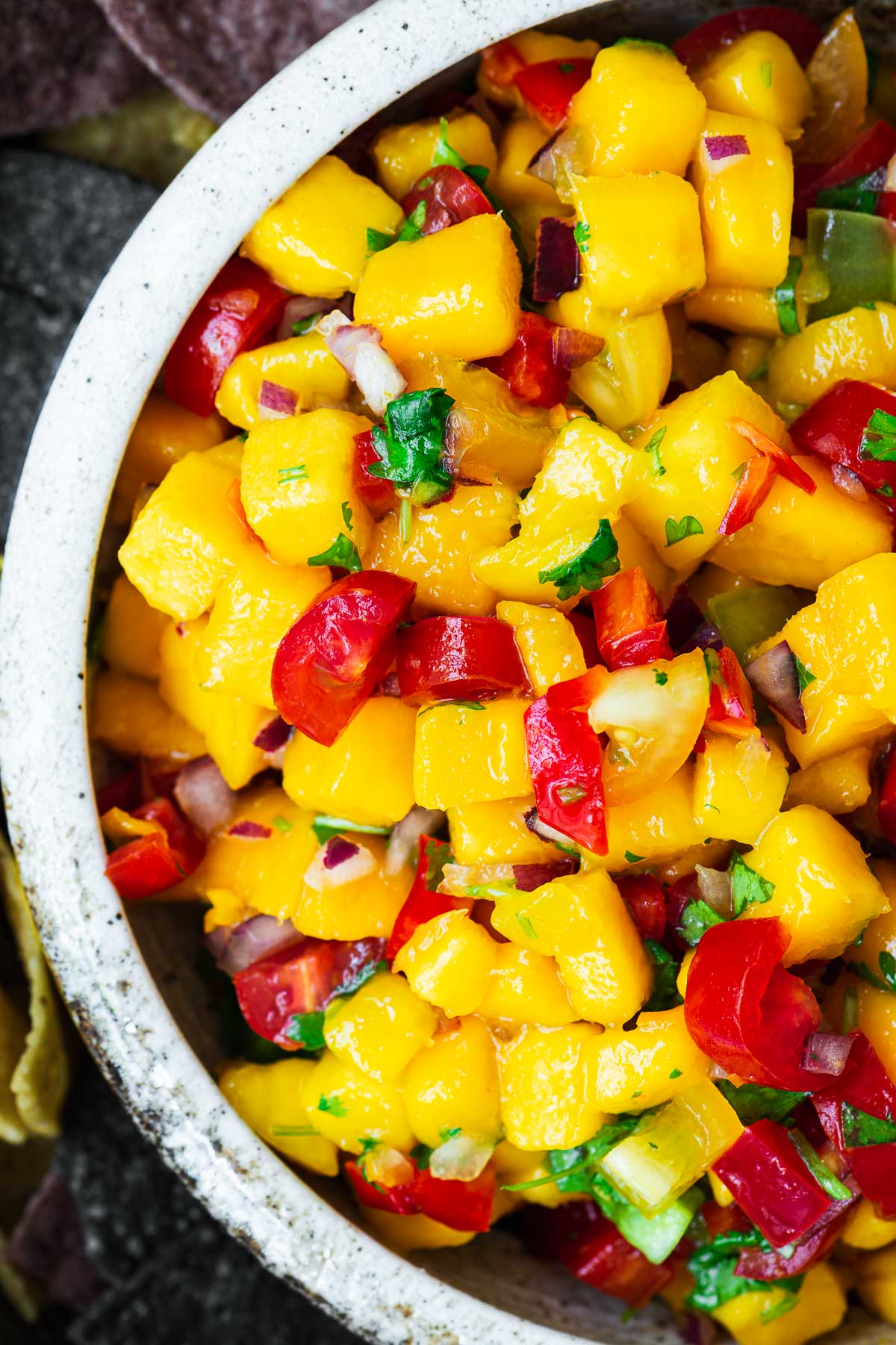 A top-down close-up view of a bowl of fresh mango habanero salsa.