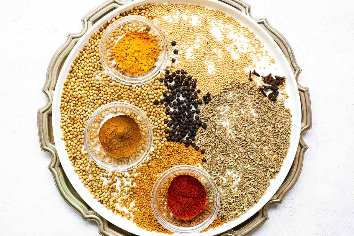 A mix of whole and ground spices typically used in Indian spice blends spread over a white plate.