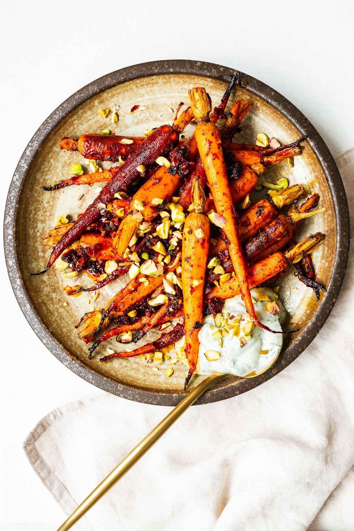 Harissa roasted carrots with chopped pistachios and a dollop of dill yoghurt in a brown ceramic serving plate.