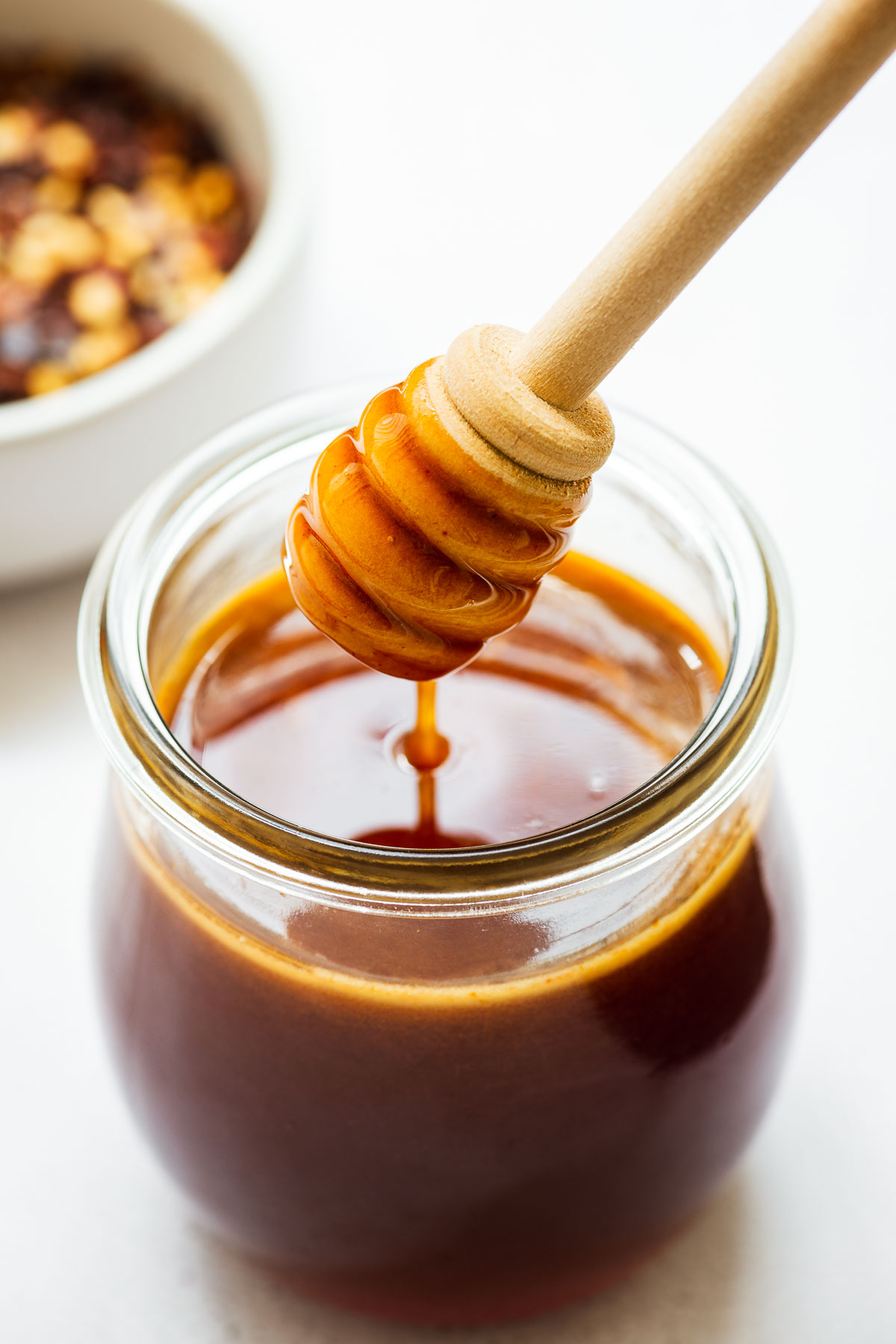 A close-up of hot honey sauce in a small glass jar with a honey dipper stick.