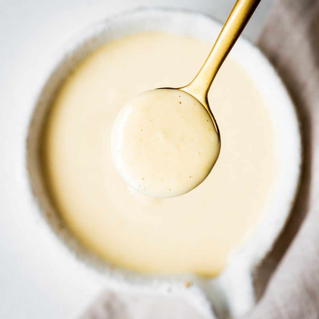 Creamy maple tahini dressing in a golden spoon viewed from above.