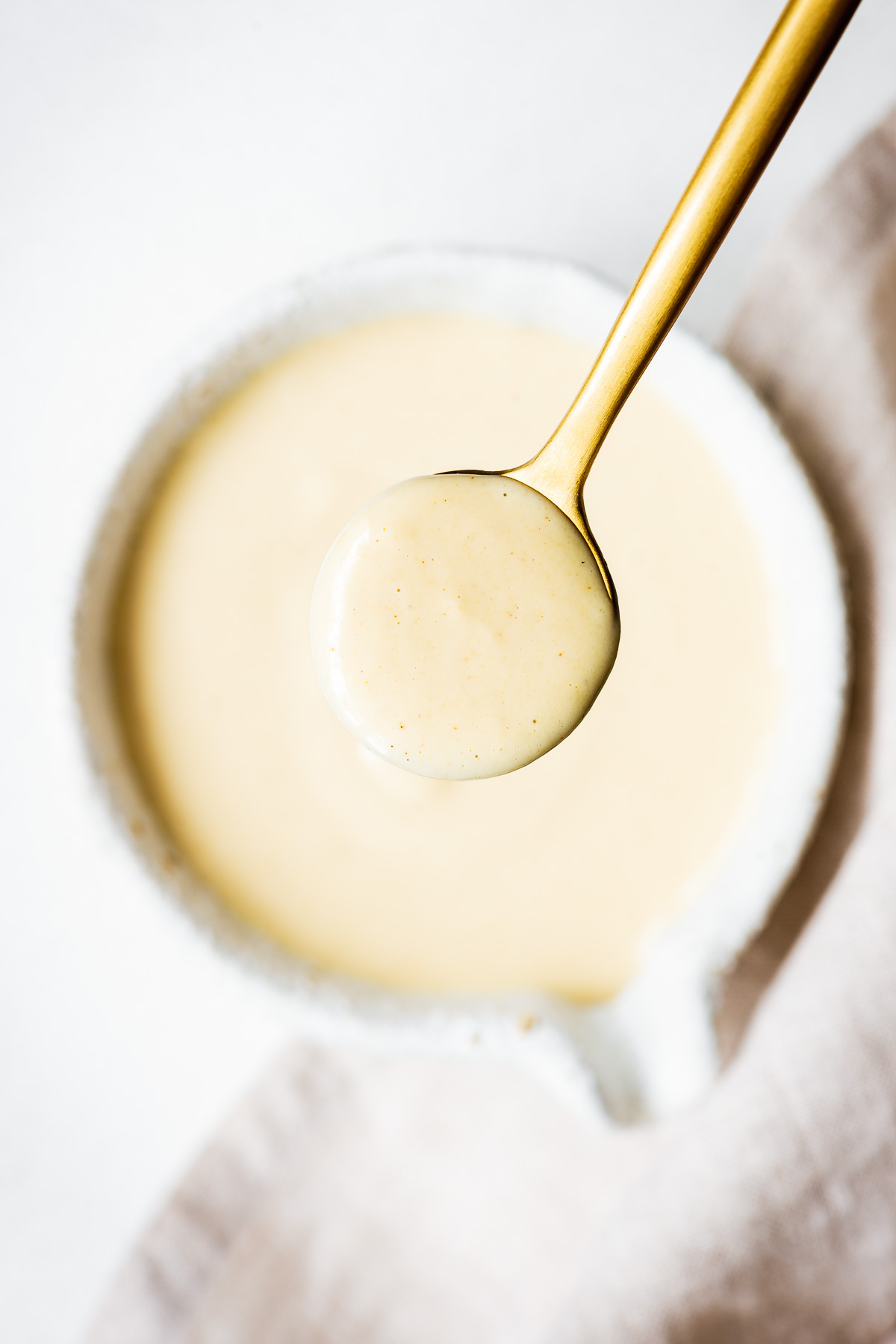 Creamy maple tahini dressing in a golden spoon viewed from above.