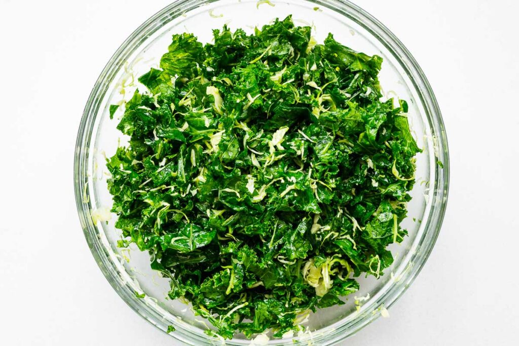A large bowl of raw kale leaves massaged with olive oil and salt to soften.