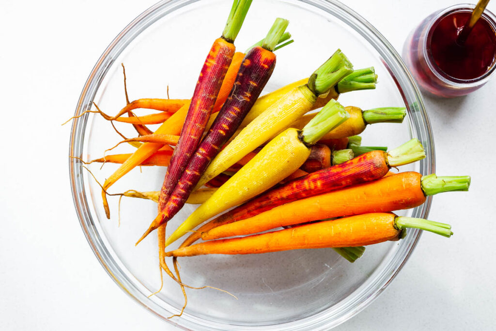 Prepared rainbow carrots in a large mixing bowl, ready to be tossed in a harissa maple marinade.