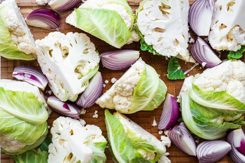 Cauliflower and onion wedges on a cutting board.