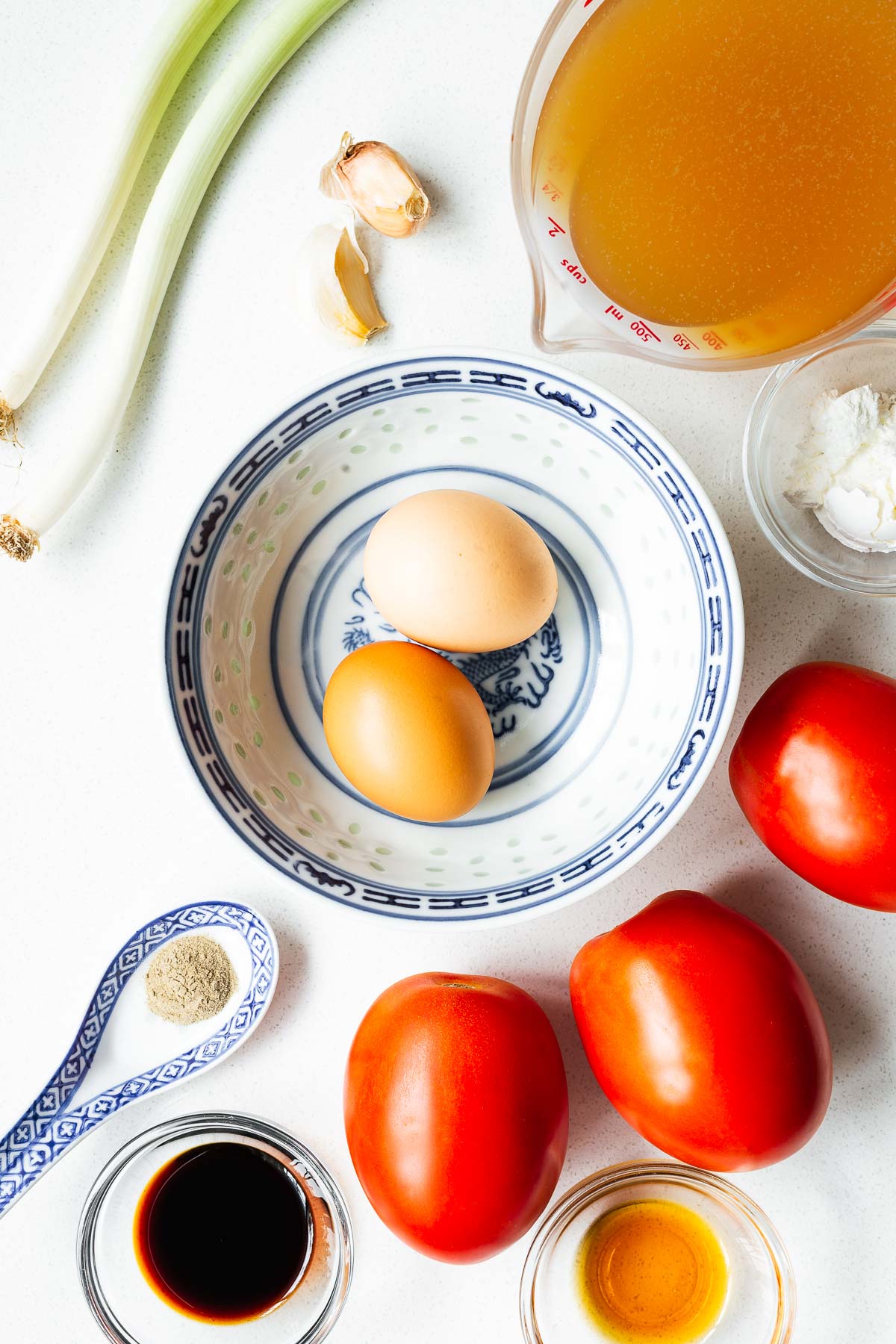 Ingredients for tomato egg drop soup arranged on a white kitchen counter viewed from above.