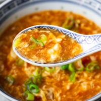 A close-up view of a spoonful of delicate egg ribbons over a bowl of tomato egg drop soup.