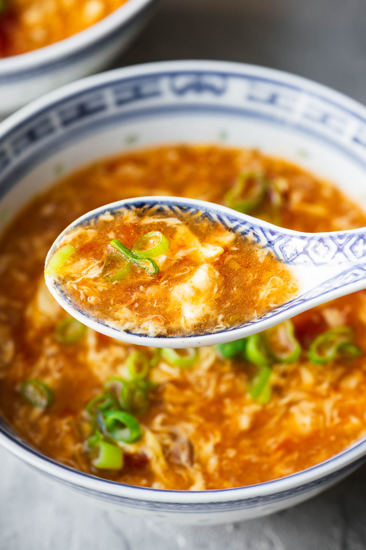 A close-up view of a spoonful of delicate egg ribbons over a bowl of tomato egg drop soup.