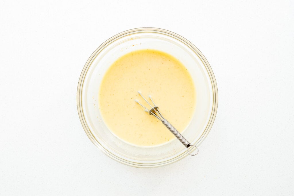 Whisked hummus dressing with a small whisk in a glass mixing bowl.