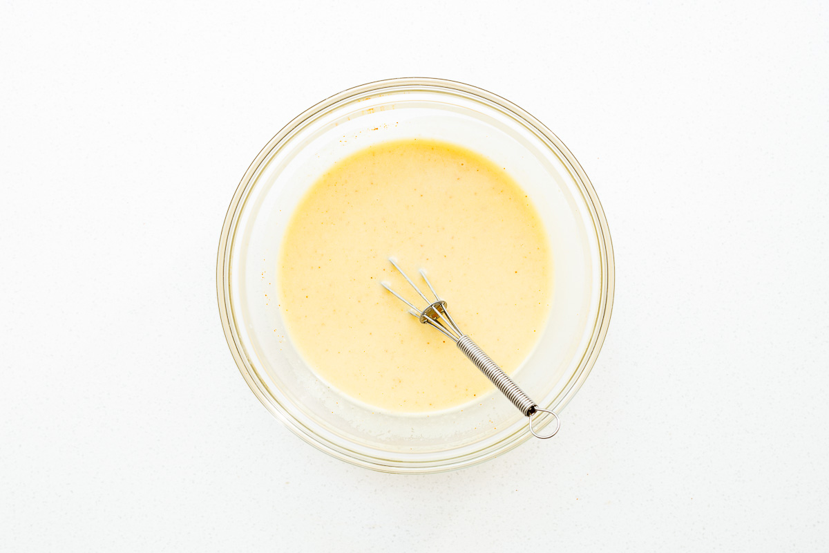 Whisked hummus dressing with a small whisk in a glass mixing bowl.