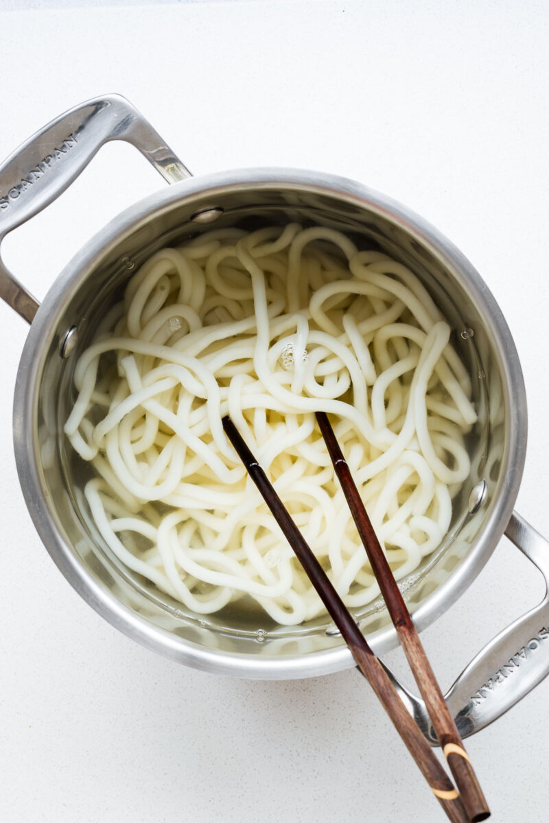 Cook udon noodles in a pot then use chopsticks to separate the noodles.