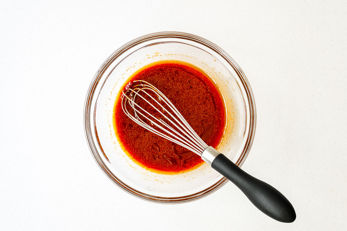 Gochujang noodle sauce in a small glass bowl with a whisk.