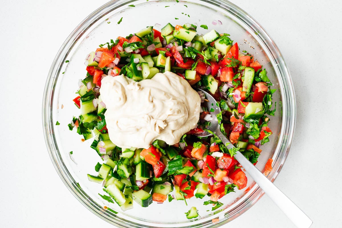 Israeli chopped salad (Jerusalem salad) topped with tahini sauce in a glass bowl before mixing.