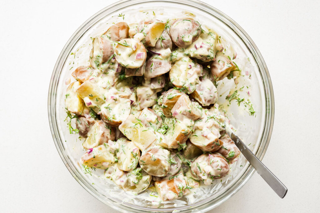 Gently folding the cooked potatoes through the creamy dressing in a large mixing bowl.