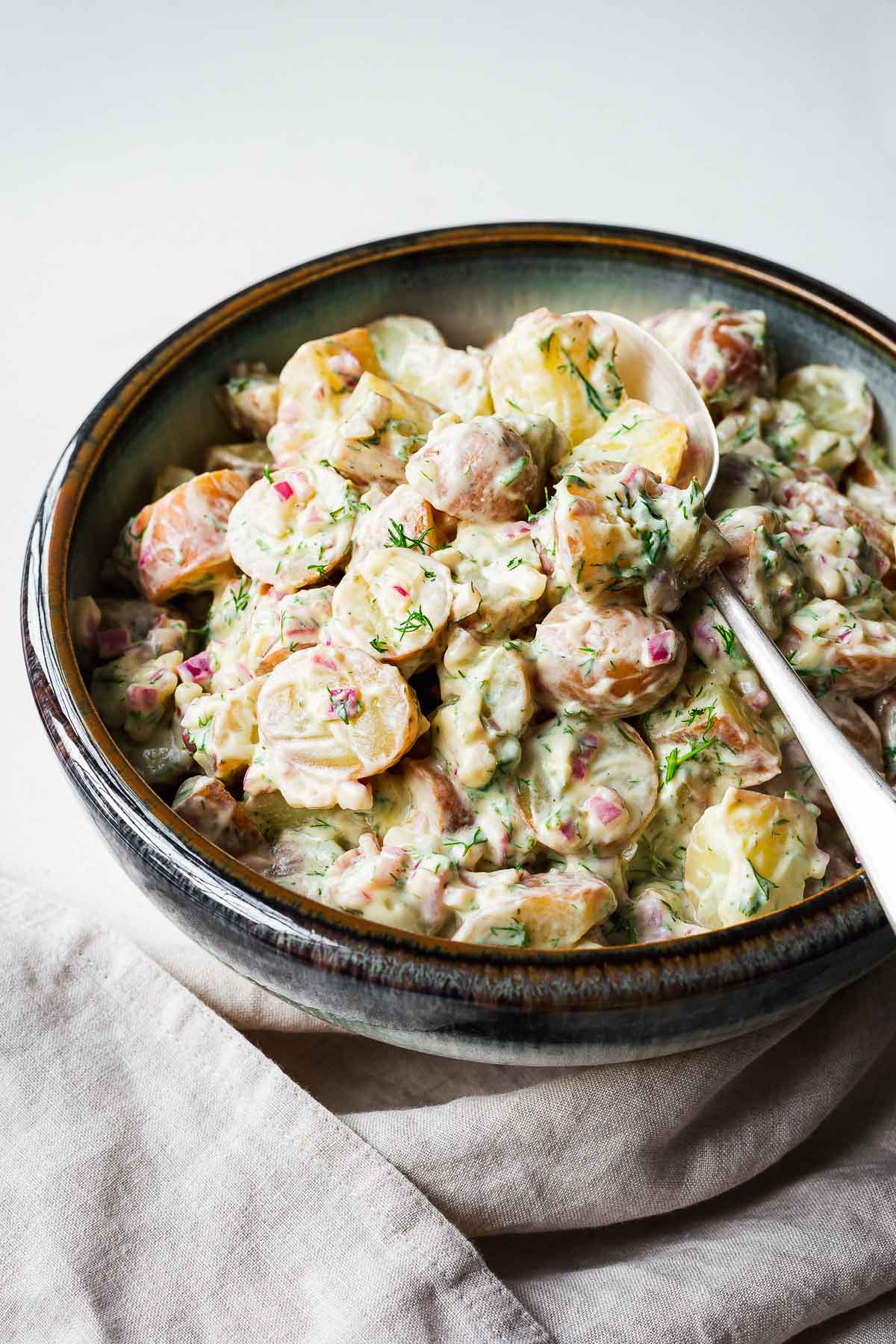 Red potato salad with dill and a creamy dressing in a serving bowl with silver spoon.