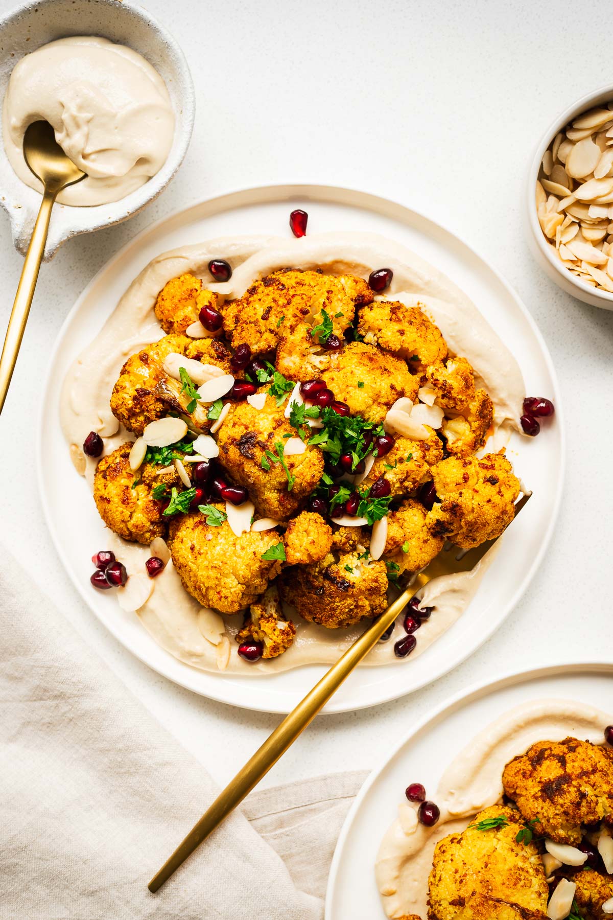 Roasted cauliflower florets on top of creamy tahini sauce with pomegranate, flaked almonds and fresh parsley on a serving plate.