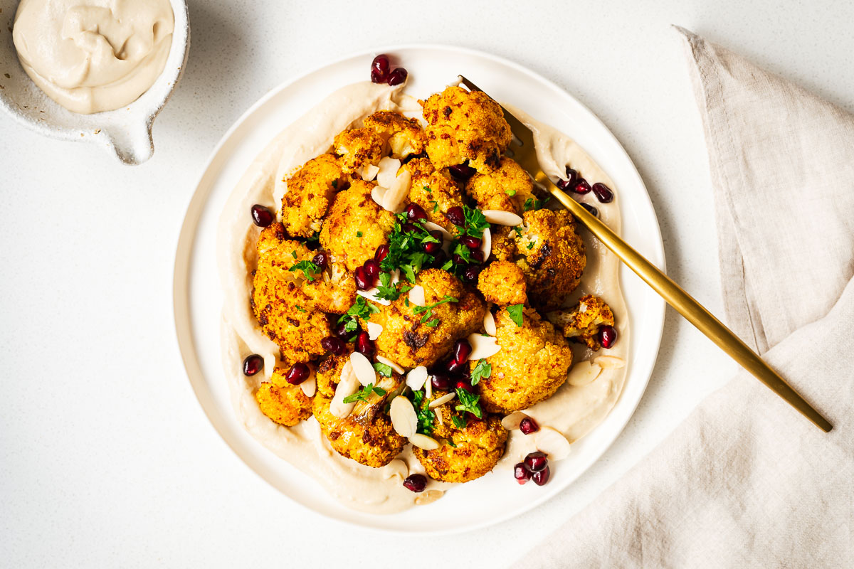 Shawarma cauliflower plated on creamy tahini sauce with a gold fork and neutral linen napkin.