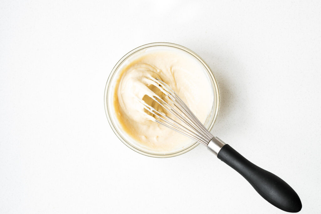 Tahini sauce for Israeli salad in a small mixing bowl with a whisk.