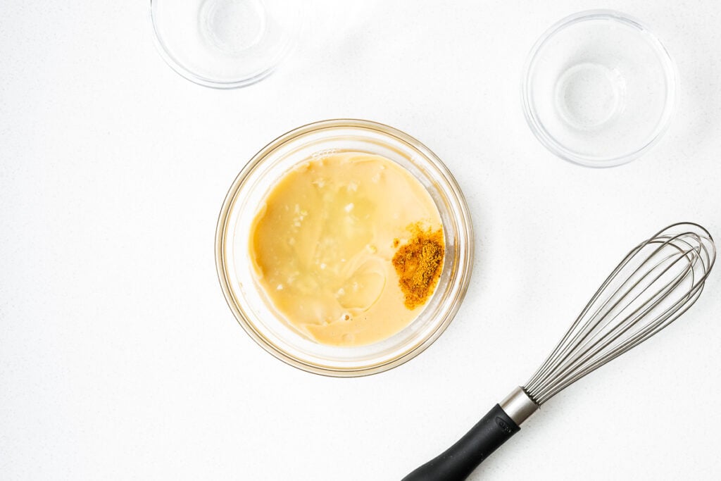 Tahini sauce ingredients in a small glass bowl next to an unused whisk.