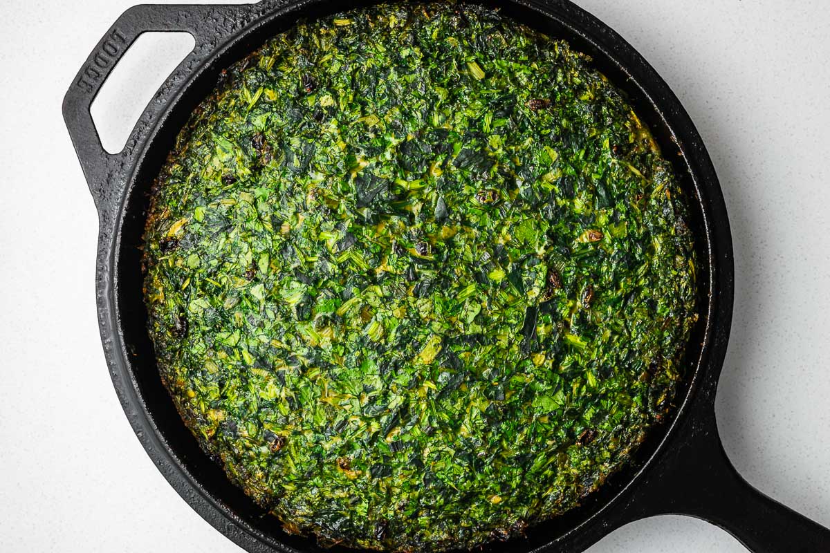 A vibrant green baked kuku sabzi in a cast-iron skillet.