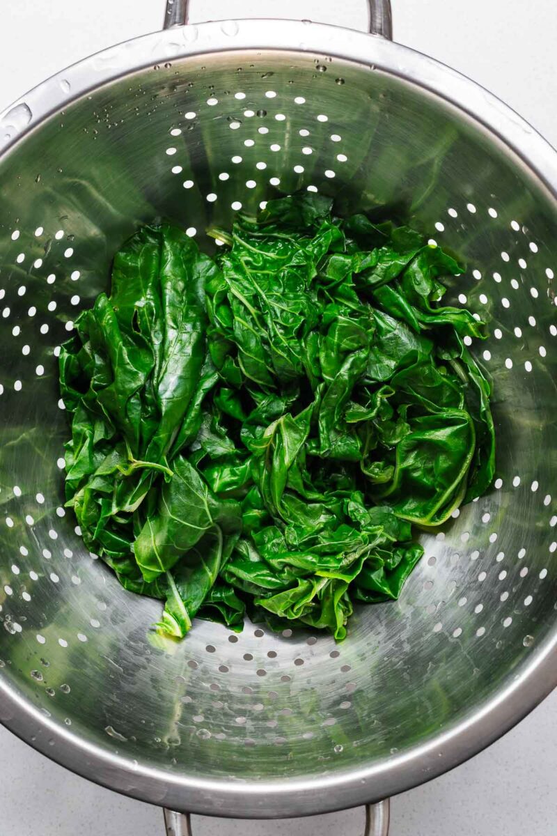 Blanched Swiss chard leaves in a colander viewed from above.