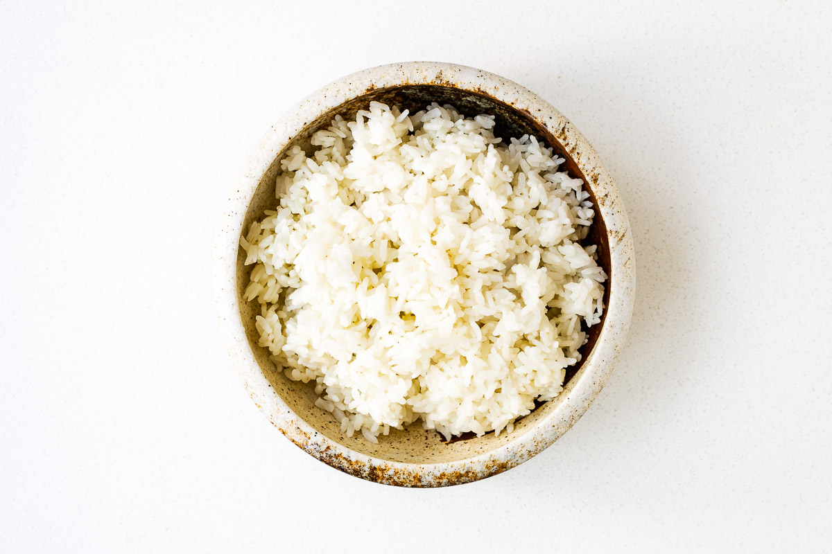 A ceramic bowl with cooked medium-grain white rice.
