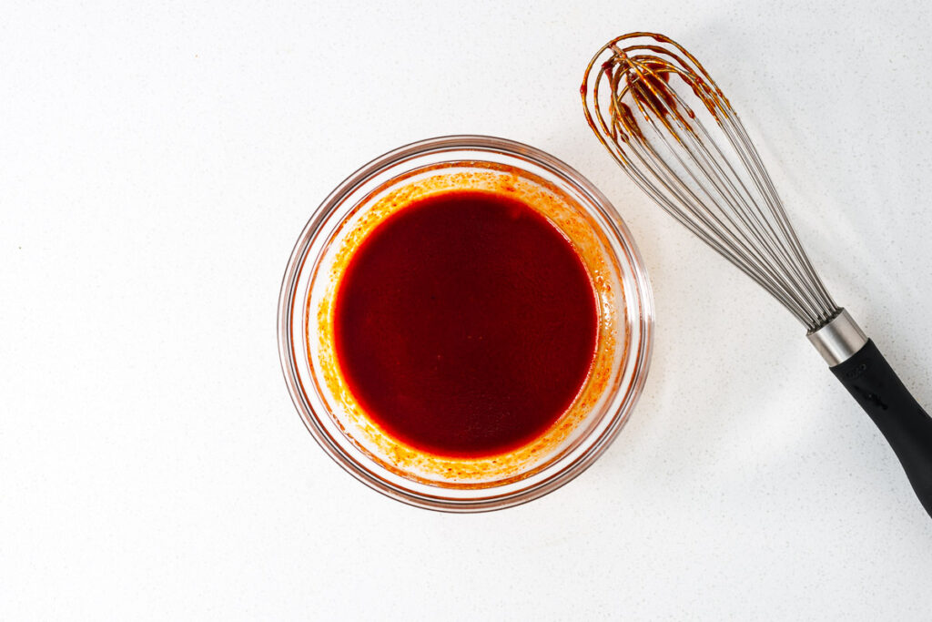 A small bowl with gochujang sauce next to a wire whisk.