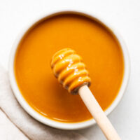 Hot honey mustard (made from Dijon mustard, hot honey, vinegar and salt) in a small bowl with a honey dipper stick.