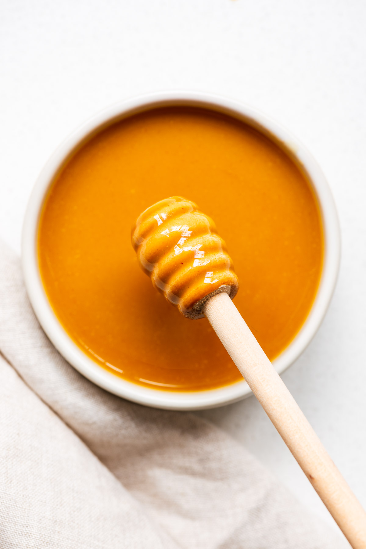 Hot honey mustard (made from Dijon mustard, hot honey, vinegar and salt) in a small bowl with a honey dipper stick.