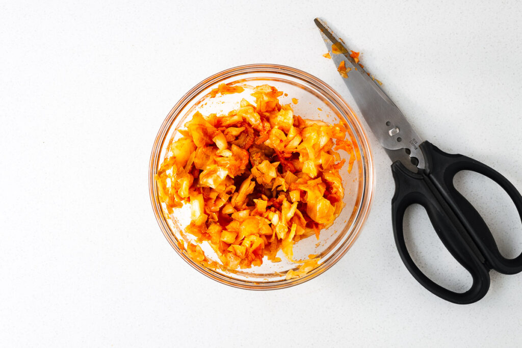 A bowl of sliced kimchi next to a pair of scissors.
