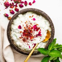 Mast-o khiar (Persian cucumber and yoghurt) in a brown ceramic bowl topped with pink edible rose petals.