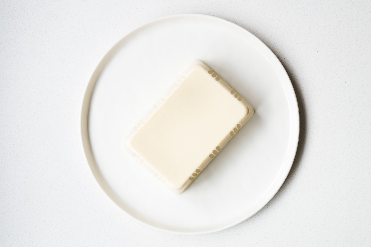 A smooth block of silken tofu on a white plate viewed from above.