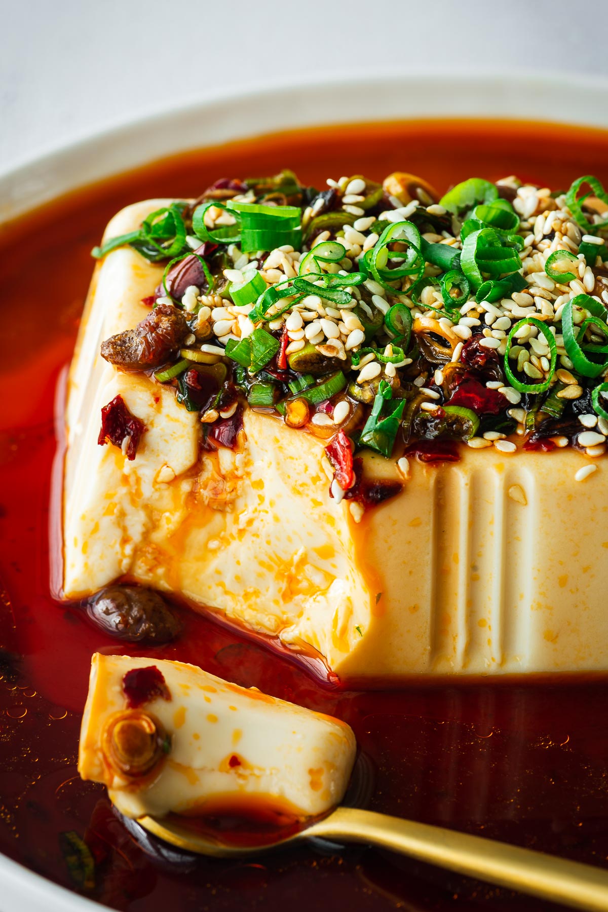 A golden spoon with a bite of silken tofu with soy-based spicy dressing.