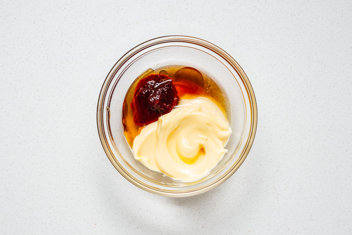 The ingredients for spicy Korean mayonnaise in a small glass bowl including kewpie mayo, gochujang, toasted sesame oil, rice vinegar and maple syrup.