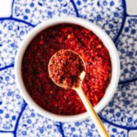 Easy Aleppo pepper substitute in a small white bowl with a golden teaspoon.