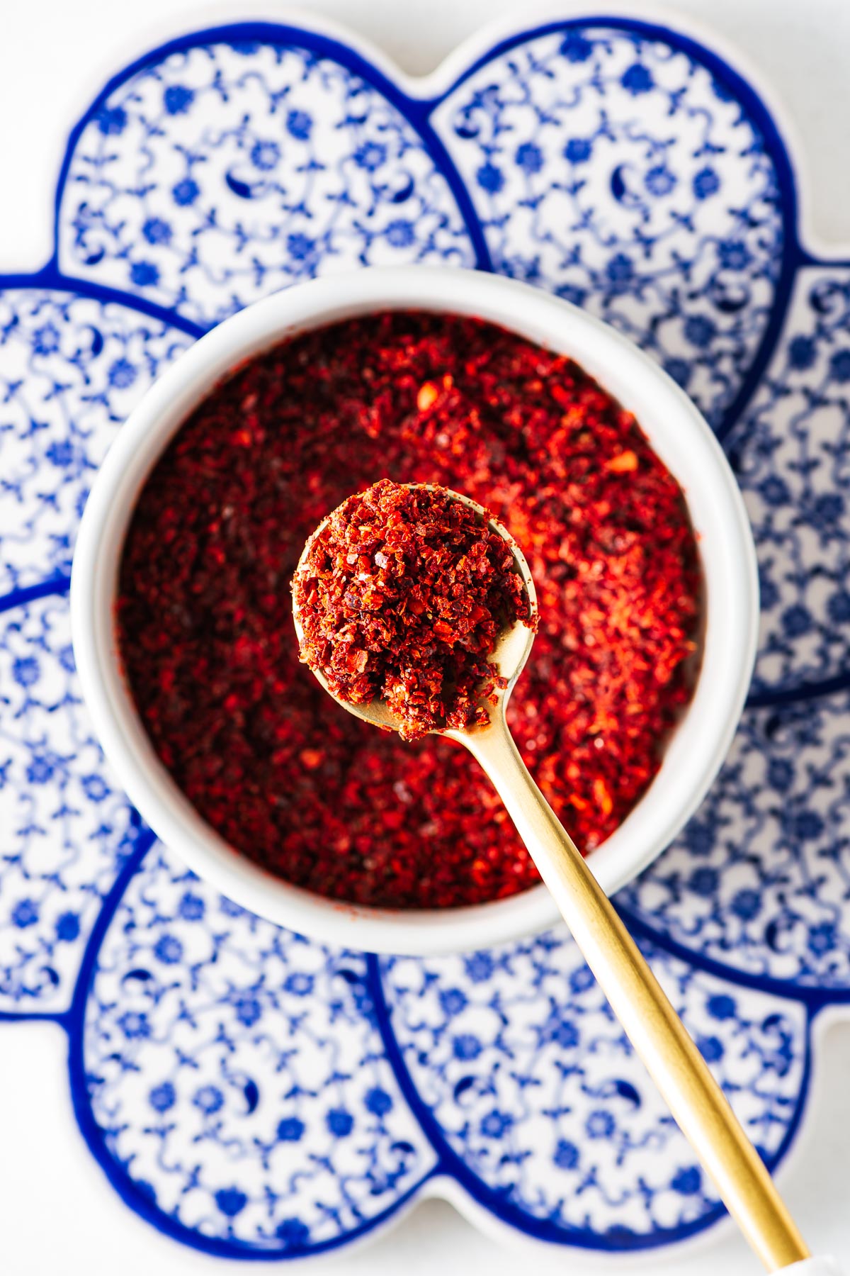 Homemade Aleppo-style pepper substitute in a small white bowl with a golden teaspoon.