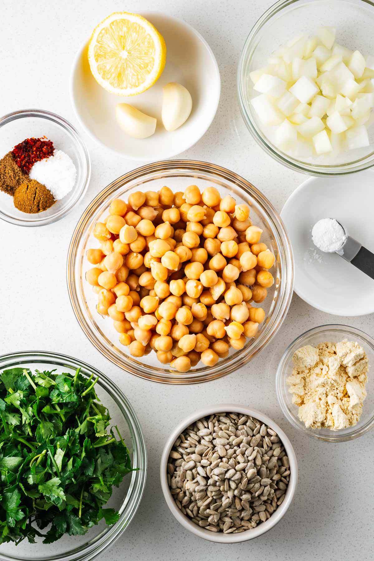 Ingredients for the baked falafel recipe using canned chickpeas arranged on a white kitchen counter viewed from above.