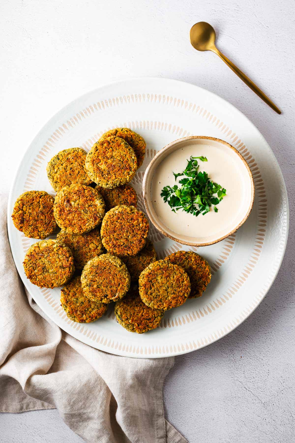 A white serving bowl with baked falafel and tahini sauce viewed from above.