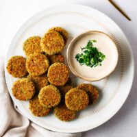 Baked falafel patties on a white serving plate with falafel sauce in a small bowl.