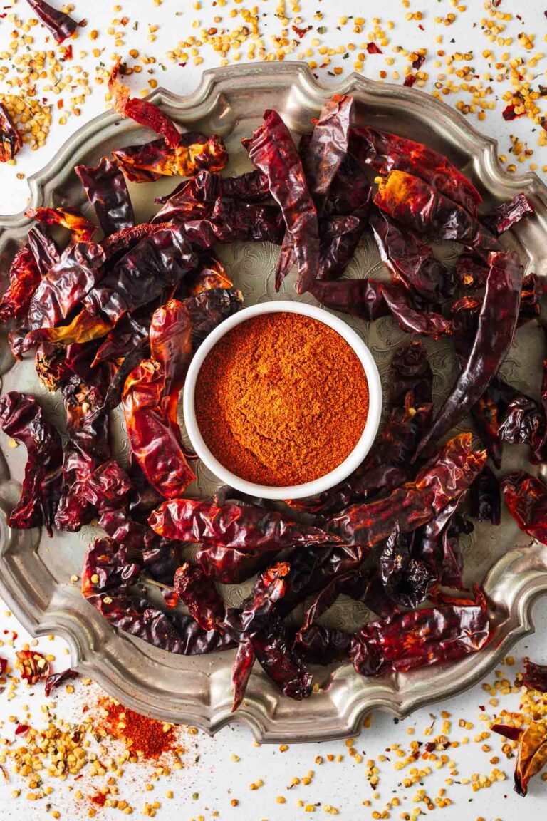 A bowl of ground cayenne pepper surrounded by dried peppers on a serving tray viewed from above.